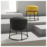 Deux tabourets modernes, l’un jaune, l’autre gris, avec des coussins ronds et des cadres en métal noir, positionnés sur une plate-forme grise minimaliste.