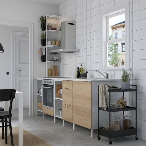 Cuisine moderne avec carrelage blanc, évier, four, armoires et un chariot noir avec bocaux et serviette. À proximité, une table à manger et une chaise.
