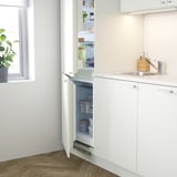 Cuisine minimaliste avec réfrigérateur intégré, évier et rangement. Armoires blanches, évier en acier inoxydable.