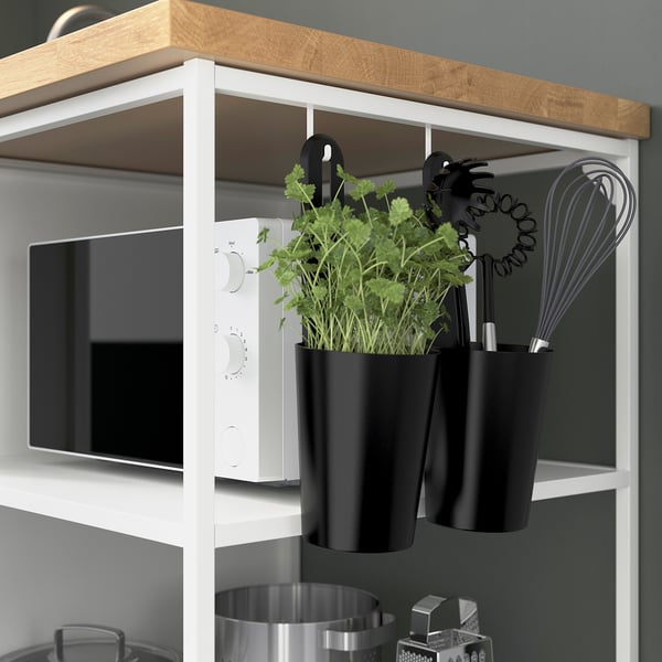 Cuisine avec étagère murale ENHET avec jardinière suspendue et ustensiles, à côté d’un micro-ondes. Cuisine propre et organisée avec rangement fonctionnel.