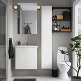 Salle de bain moderne et minimaliste avec meuble-lavabo ENHET blanc, miroir et toilettes. Des murs gris, des accents sombres et une plante en pot.