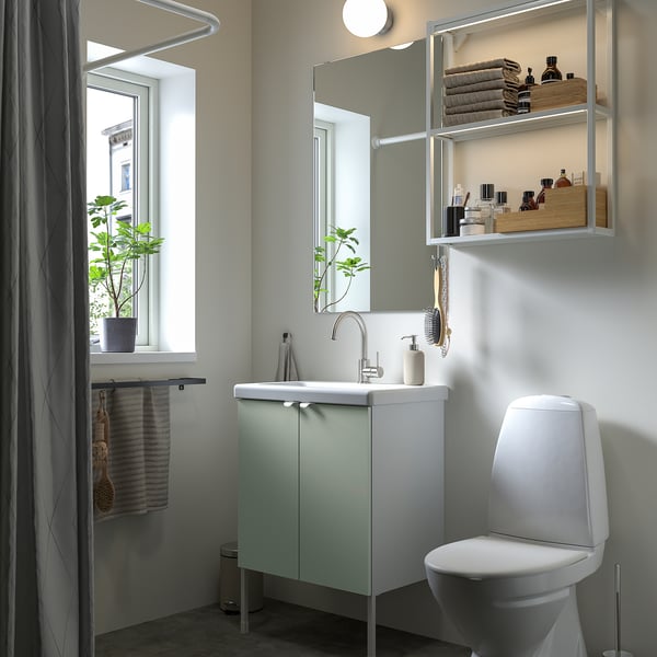 Salle de bain contemporaine avec vanité ENHET vert clair, toilettes blanches, miroir avec étagères. Des serviettes et des plantes décorent un espace soigneusement organisé.