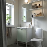 Salle de bain contemporaine avec vanité ENHET vert clair, toilettes blanches, miroir avec étagères. Des serviettes et des plantes décorent un espace soigneusement organisé.