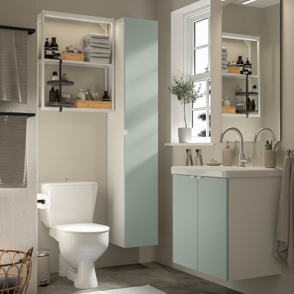Salle de bain moderne avec rangement gris-vert ENHET, armoire haute, cadre mural et lavabo. Étagères organisées, miroir et fenêtre.