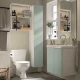 Salle de bain moderne avec rangement gris-vert ENHET, armoire haute, cadre mural et lavabo. Étagères organisées, miroir et fenêtre.