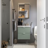 Salle de bain moderne avec meuble ENHET. Miroir coulissant, accessoires noirs, serviettes grises. Toilette blanche, douche.