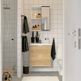 Salle de bain moderne avec vanité en bois clair, carreaux blancs, accents noirs, douche en verre et armoire de toilette.