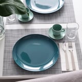 Mise en place de la table avec des assiettes, des tasses et des couverts bleus sur des sets de table.