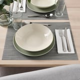 Deux couverts avec bols, couverts et verres sur des sets de table tissés.