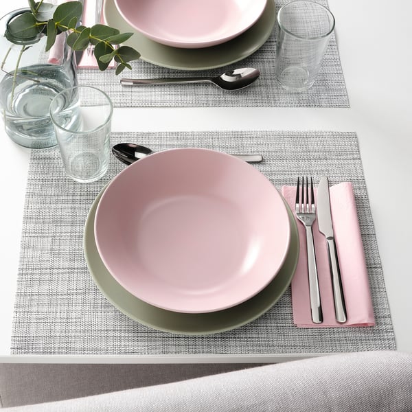 Deux couverts avec des bols roses et verts, de l’argenterie, des verres et des sets de table tissés sur une table blanche.