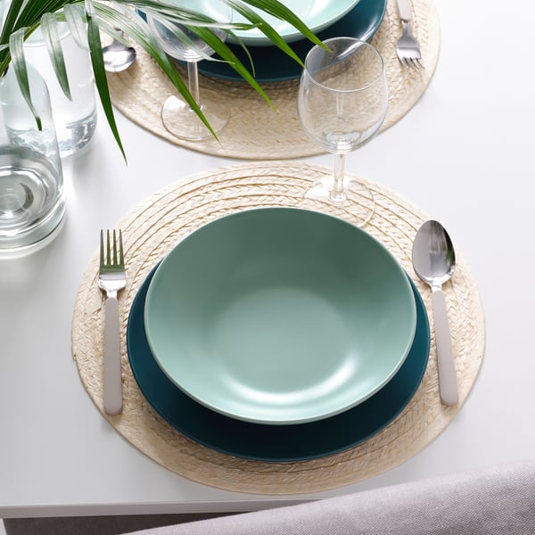 Table avec des assiettes vert foncé FÄRGKLAR, des sets de table naturels, de l’argenterie et des verres.