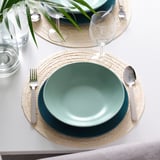 Table avec des assiettes vert foncé FÄRGKLAR, des sets de table naturels, de l’argenterie et des verres.