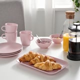 Une table dressée avec des assiettes roses, des tasses, des bols, des croissants et une cafetière ; Prêt pour un petit-déjeuner.