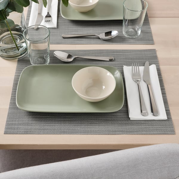 Set de table avec de la vaisselle verte et blanche, des tasses en verre, de l’argenterie et des sets de table gris.