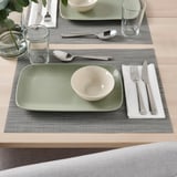 Set de table avec de la vaisselle verte et blanche, des tasses en verre, de l’argenterie et des sets de table gris.