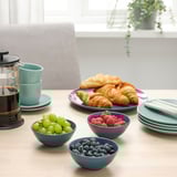 Une table de petit-déjeuner avec des viennoiseries, des fruits frais et du café dans des bols et des tasses turquoise, prêts pour un repas.
