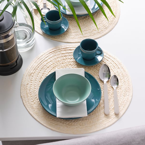 Table dressée avec des assiettes bleues, des bols, des tasses, des cuillères, des serviettes et une théière.