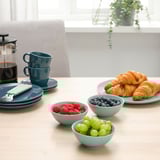 Table bleue avec des fruits, du café et des pâtisseries près d’une fenêtre.