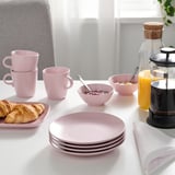 Table dressée avec des assiettes roses, des bols, des tasses, des croissants, du jus de fruits et une cafetière.