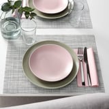 Dressage de table avec des assiettes roses et vertes, des verres transparents et des serviettes roses sur des sets de table texturés.