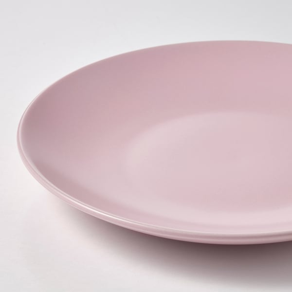 Assiette lisse rose clair avec une surface légèrement texturée, exposée sur un fond blanc.
