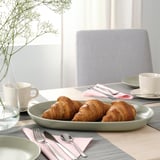 Configuration du petit-déjeuner avec croissants sur une assiette, tasses, serviettes et argenterie sur une table en bois.