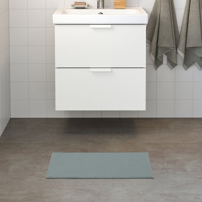 Petit tapis FINTSEN bleu clair devant meuble-lavabo blanc.