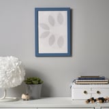 Un bureau moderne avec une photo encadrée de bleu, une plante en pot, une lampe blanche et des livres empilés, montrant une configuration de décoration minimaliste.
