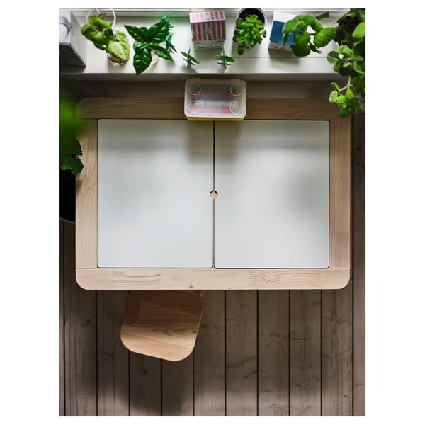 Table d’enfant moderne, blanc et bois. L’étagère supérieure contient des plantes vertes et des jouets. La table a des portes givrées et un design minimaliste.