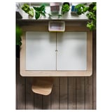 Table d’enfant moderne, blanc et bois. L’étagère supérieure contient des plantes vertes et des jouets. La table a des portes givrées et un design minimaliste.