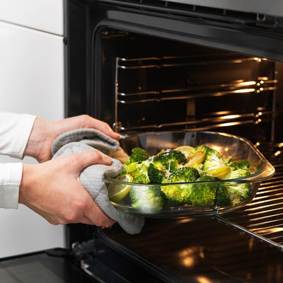 Personne plaçant un plat en verre avec du brocoli dans le four. Les poignées permettent de soulever facilement.