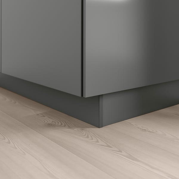 Un socle de cuisine moderne en gris foncé, placé au coin d’un plancher en bois, offrant une finition sans couture aux armoires basses.