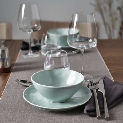Bol et assiette en porcelaine gris turquoise, avec verres à vin et couverts sur une table.
