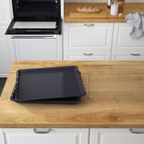 Scène de cuisine avec four ouvert montrant une plaque de cuisson noire vide et une grille sur un comptoir en bois.