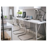 Bureau à domicile moderne avec bureau blanc, chaises transparentes et lampe élégante. Des murs gris clair, des planchers en bois et une couverture douillette.
