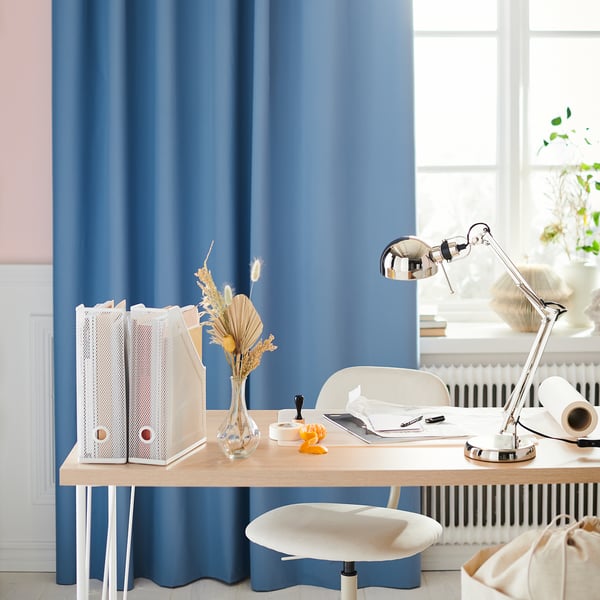 Bureau à domicile moderne avec rideaux bleus, bureau en bois, chaise blanche et lampe FORSÅ argentée réglable.