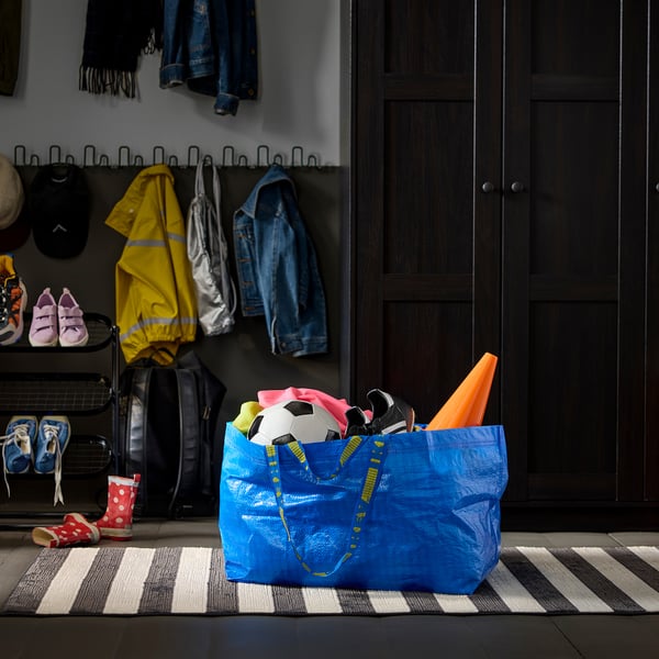 Sac à provisions réutilisable bleu rempli d’articles, dont un ballon de soccer, près d’un vestiaire avec des patères, des chaussures et des vestes.