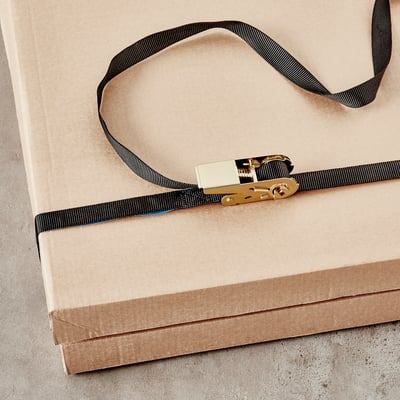 Bretelles cargo noires avec boucles métalliques fixant une boîte en carton.