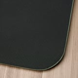Tapis debout antibactérien noir avec surface texturée et bord vert, posé sur un sol en bois.