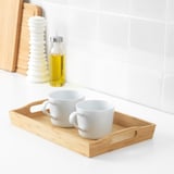 Deux tasses blanches sur un plateau en bois, avec une bouteille d’huile jaune et une salière blanche sur un comptoir carrelé.