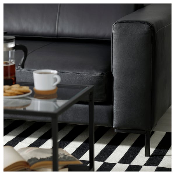 Salon moderne avec canapé FULLERÖ en cuir noir, table basse en verre avec biscuits et tasse à café.