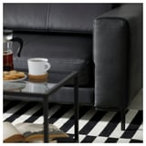 Salon moderne avec canapé FULLERÖ en cuir noir, table basse en verre avec biscuits et tasse à café.