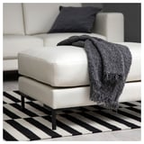 Ottoman moderne en cuir blanc avec couverture à franges noires, sur tapis à rayures noires et blanches.