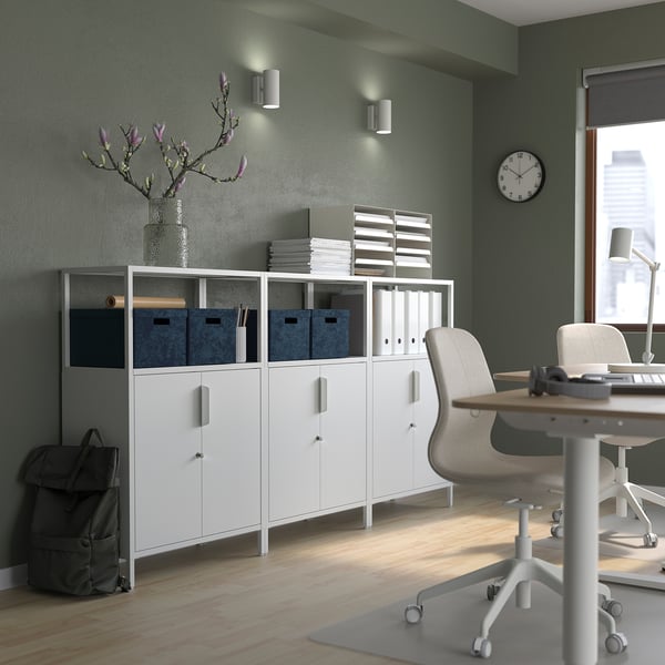 Bureau à domicile moderne avec des murs verts, des meubles blancs et des rangements GJÄTTA. Bureau, chaise et sac à dos gris en vue.