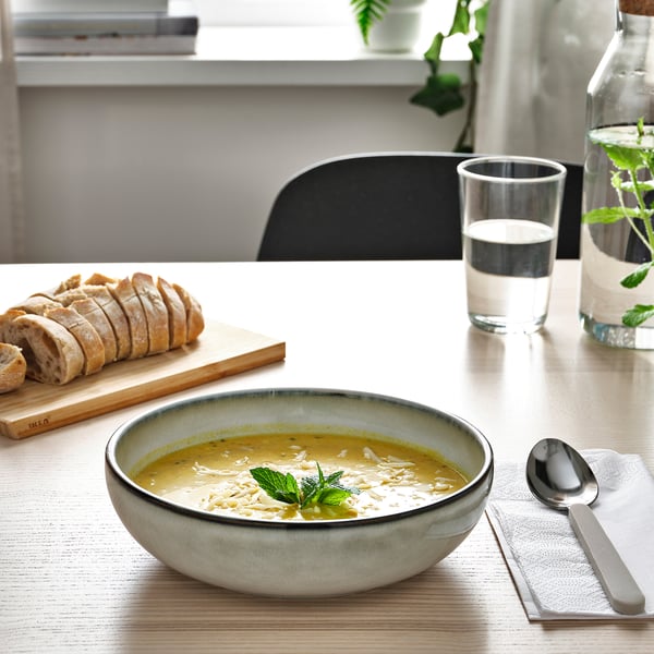 Bol de soupe et pain coupé sur la table, avec un verre d’eau et une cuillère.