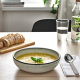 Bol de soupe et pain coupé sur la table, avec un verre d’eau et une cuillère.