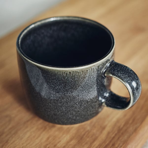 Tasse émaillée gris foncé sur surface en bois ; Toucher lisse et artisanal, fait partie de la série GLADELIG.