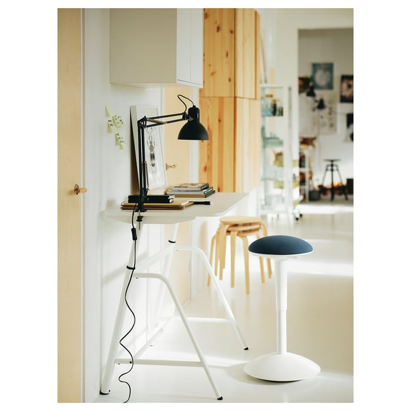 Bureau à domicile minimaliste : bureau blanc, lampe noire, moniteur, livres, tabouret bleu.