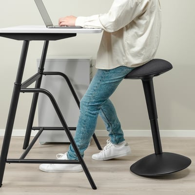 Personne assise sur un tabouret réglable, travaillant sur un bureau d’ordinateur portable qui monte ou descend. Le bureau à ressorts à gaz s’ajuste en douceur pour s’asseoir ou se tenir debout.