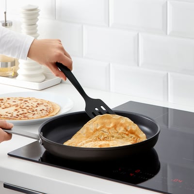 Personne cuisinant des crêpes avec des ustensiles GNARP et une spatule sur une poêle antiadhésive.